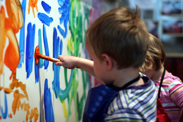 Little boy painting while a little girl watches in the background.